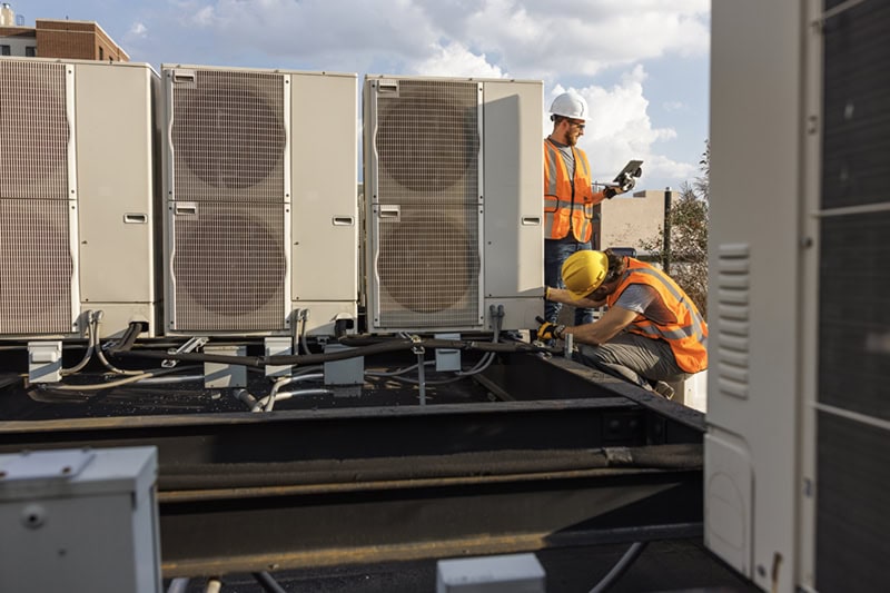 Preparing Your Commercial HVAC for Texas' Hot Summers. Photo of technicians performing a system inspection on a rooftop HVAC system.