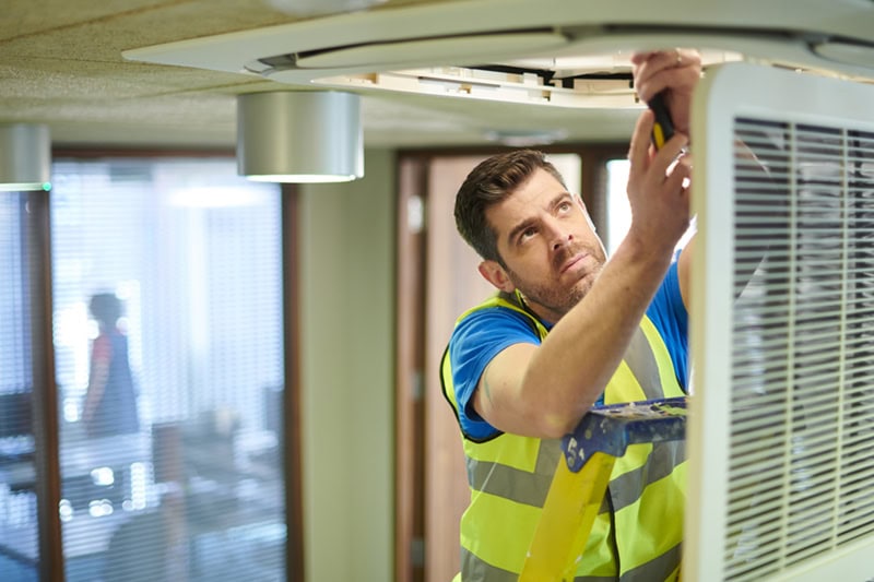 The Benefits of Finding a Commercial HVAC Company to Service All Your Properties in DFW. Photo of a technician performing maintenance on an HVAC System installed in the ceililng.